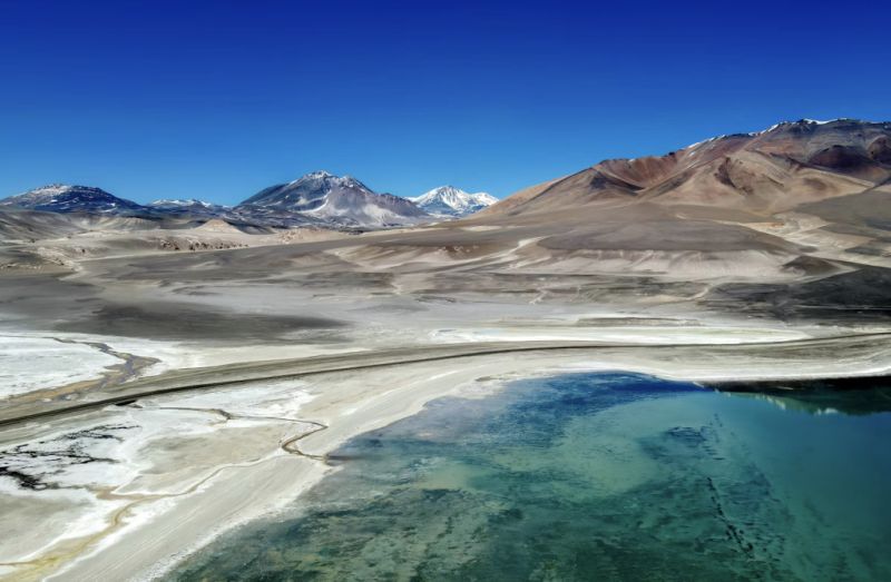 Desert valley with snow-capped mountains in the distance and a turquoise pool in the foreground.