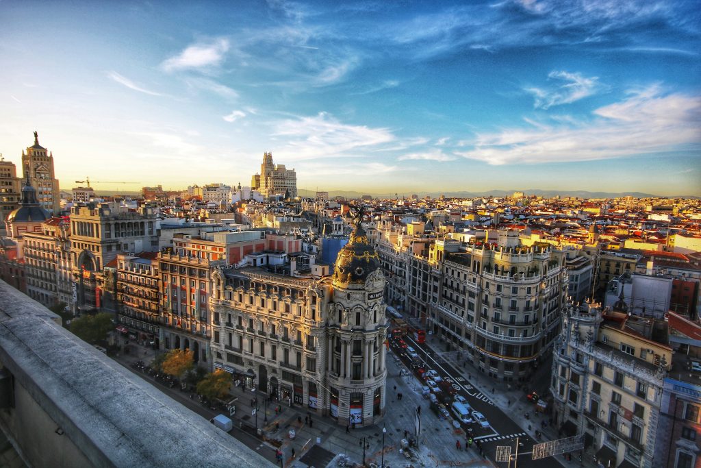 High-angle view over a European city center at sunset; ornate stone buildings line a busy street grid.